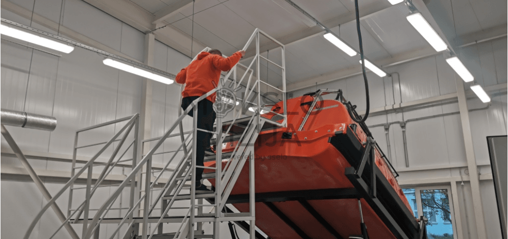 Gelbėjimosi valties treniruoklis su tikroviška kabina ir dinamine platforma, imituojantis laisvą kritimą į vandenį.