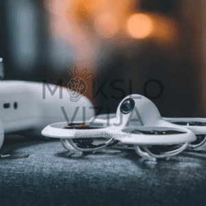 Baltas mini FPV dronas su integruota kamera padėtas ant audinio paviršiaus, šalia matomas valdymo pultas.