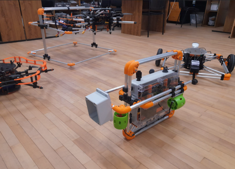 Povandeninis robotas su tvirtu rėmu ir moduliais testuojamas patalpoje ant grindų, matoma mokomoji laboratorinė aplinka.