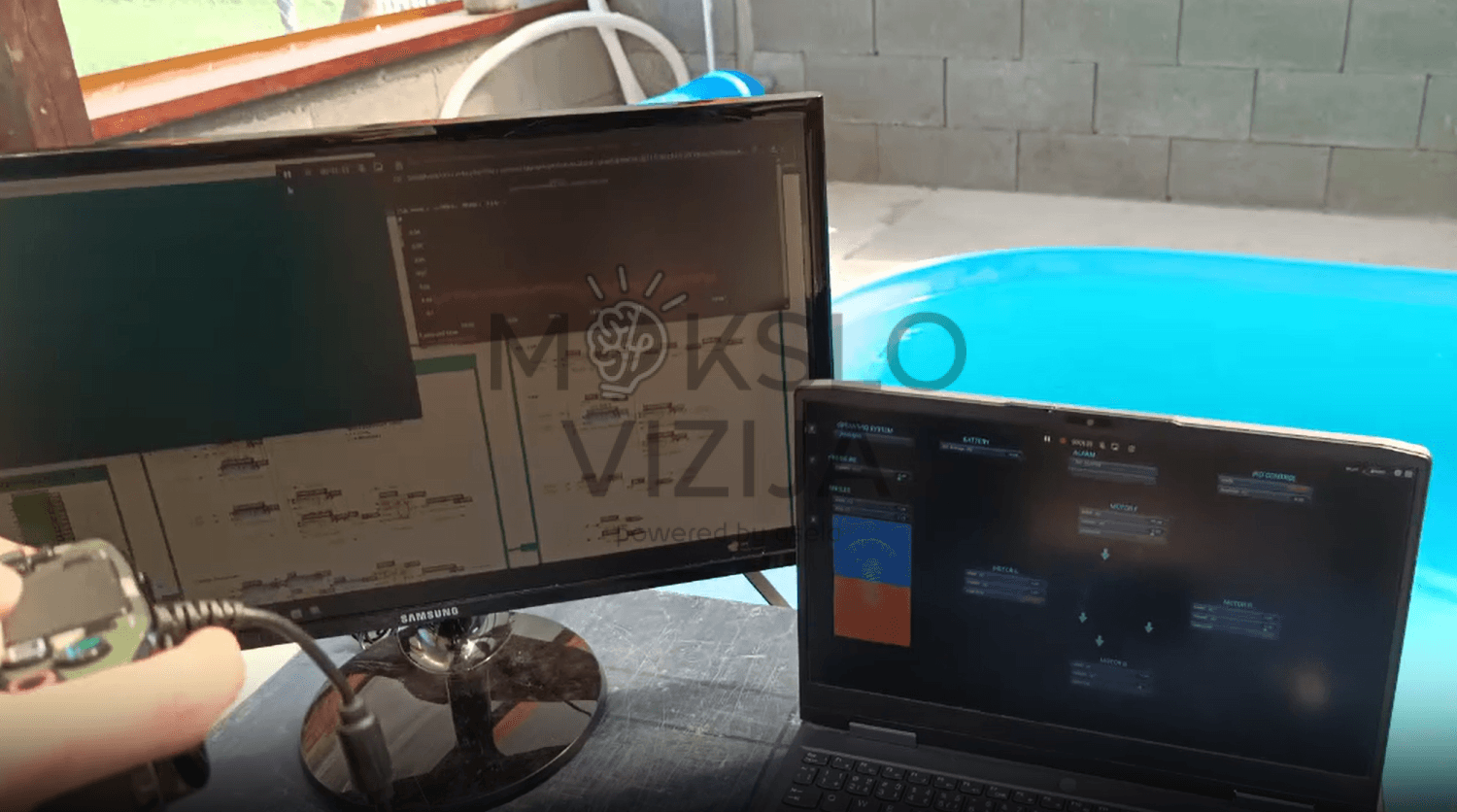 Monitorius ir nešiojamas kompiuteris rodo povandeninio roboto valdymo programą ir telemetriją šalia baseino bandymams.