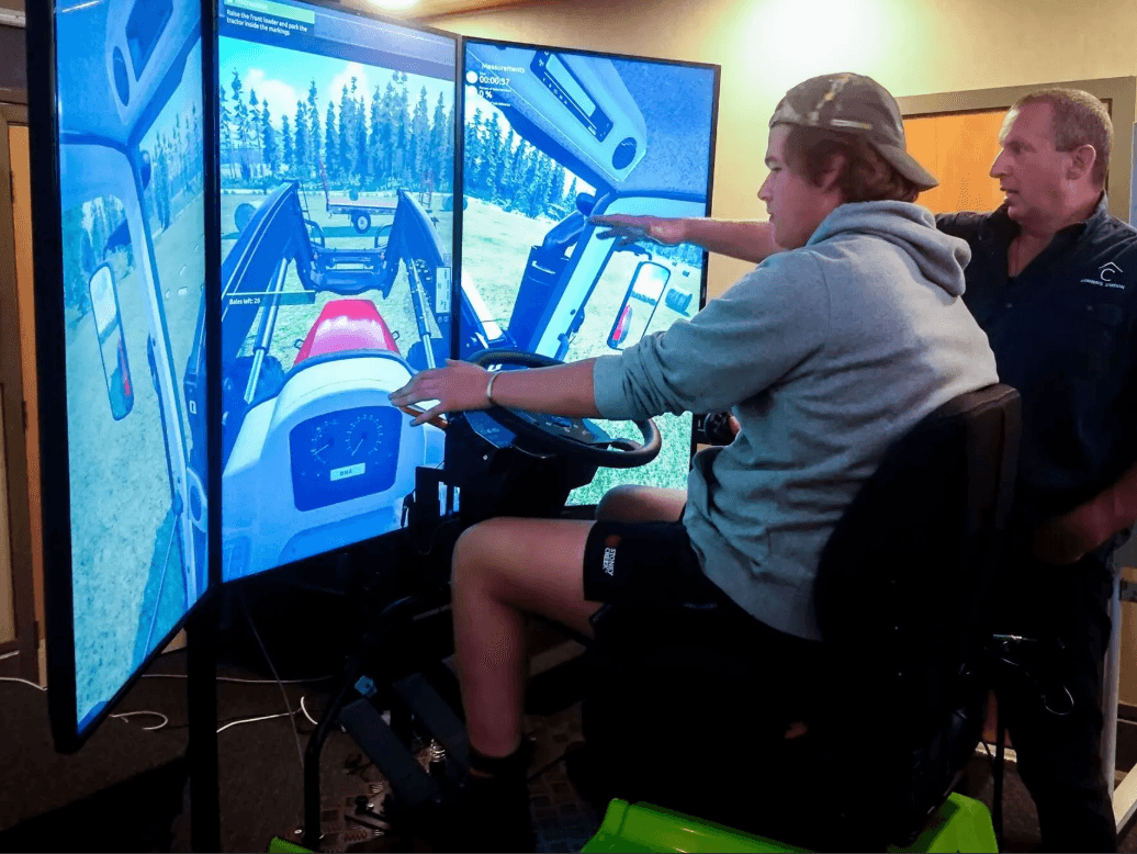 Tenstar TRACTOR (TR LI) traktoriaus vairavimo simuliatorius, keli ekranai, mokinys treniruojasi su instruktoriumi.