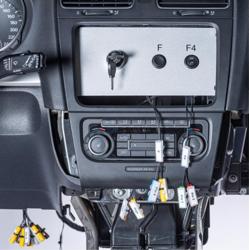 Automobilio centrinės konsolės modulis su pažymėtomis diagnostikos jungtimis ir laidais komforto sistemų mokymui.