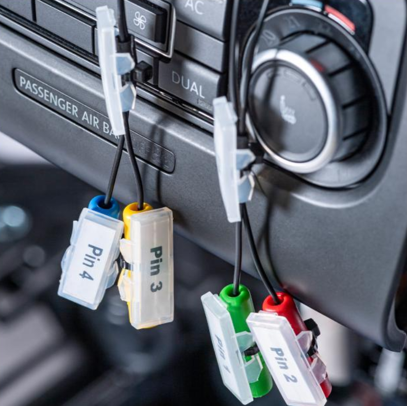 Automobilio klimato valdymo skydelis su pažymėtais diagnostikos laidais ir jungtimis mokymo stende.