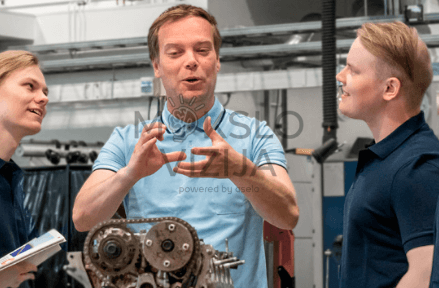 Instruktorius dirbtuvėse aiškina techninį mazgą automobilių technikų komandai.