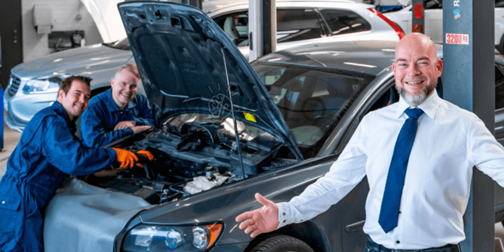 Autoservisas su atidarytu automobilio variklio dangčiu ir darbuotojais prie variklio.