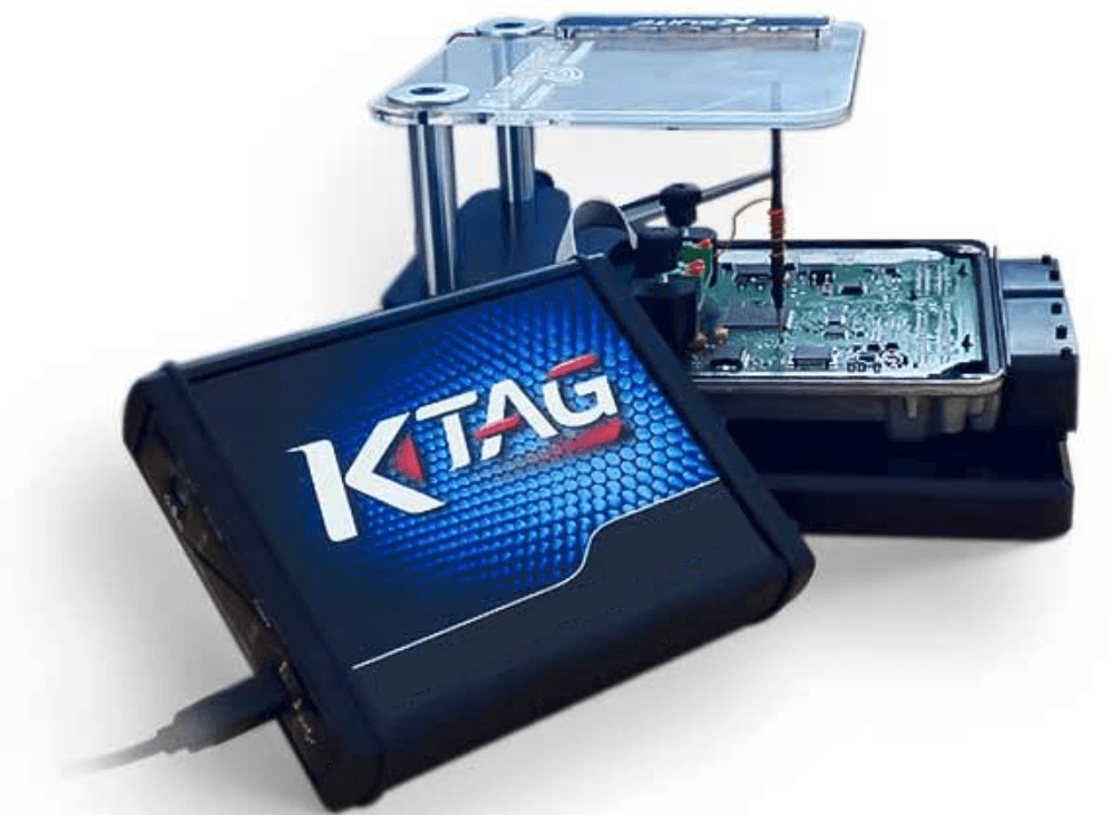 Alientech K-TAG ECU programavimo įrenginys su prijungtu kabeliu ir ECU valdymo bloku fone.