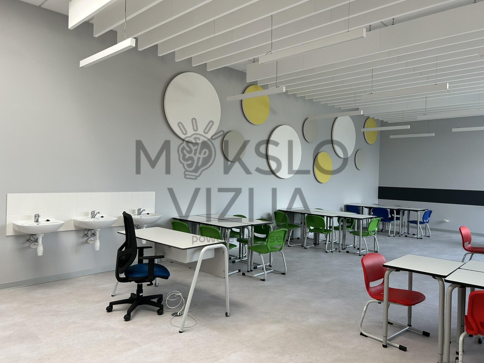 Moderni mokyklos klasė su mokinių stalais, kriauklėmis ir akustinėmis sienų panelėmis.