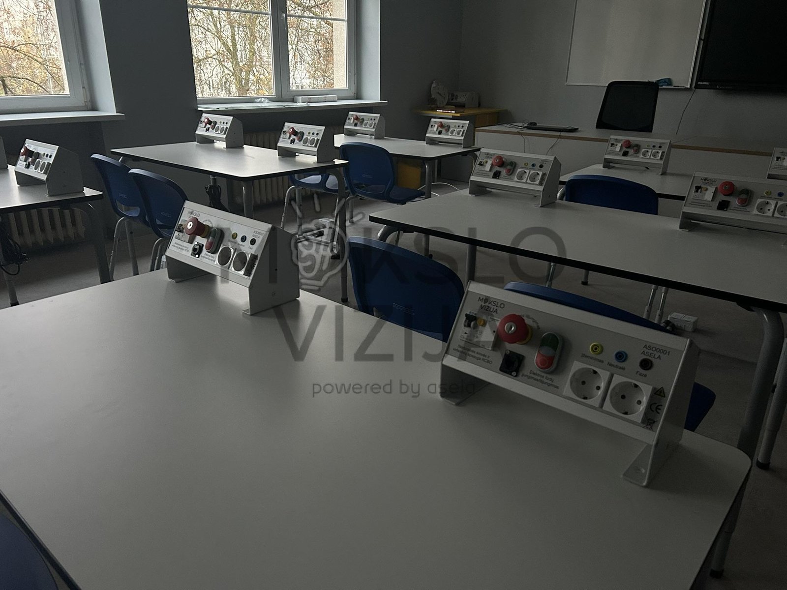 Gamtos mokslų klasė su mokinių stalais ir elektros eksperimentų valdymo moduliais.