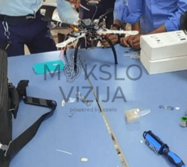 Mokiniai laboratorijoje dirba su drono surinkimu ir elektronikos komponentų testavimu ant mokomojo stalo, skirtu profesiniam dronų technologijų mokymui.