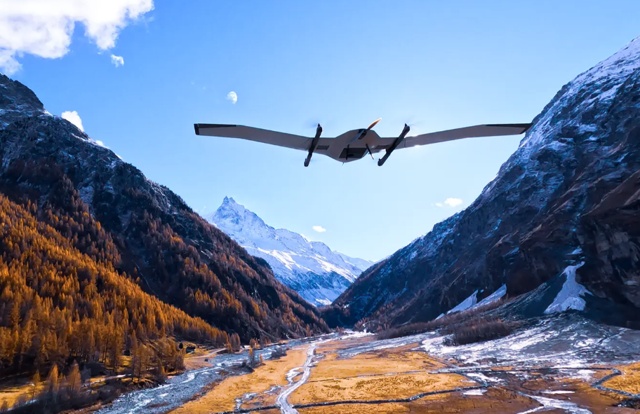 DeltaQuad Evo dronas skrydžio metu virš kalnų slėnio, naudojamas teritorijų kartografavimui ir LiDAR duomenų surinkimui.