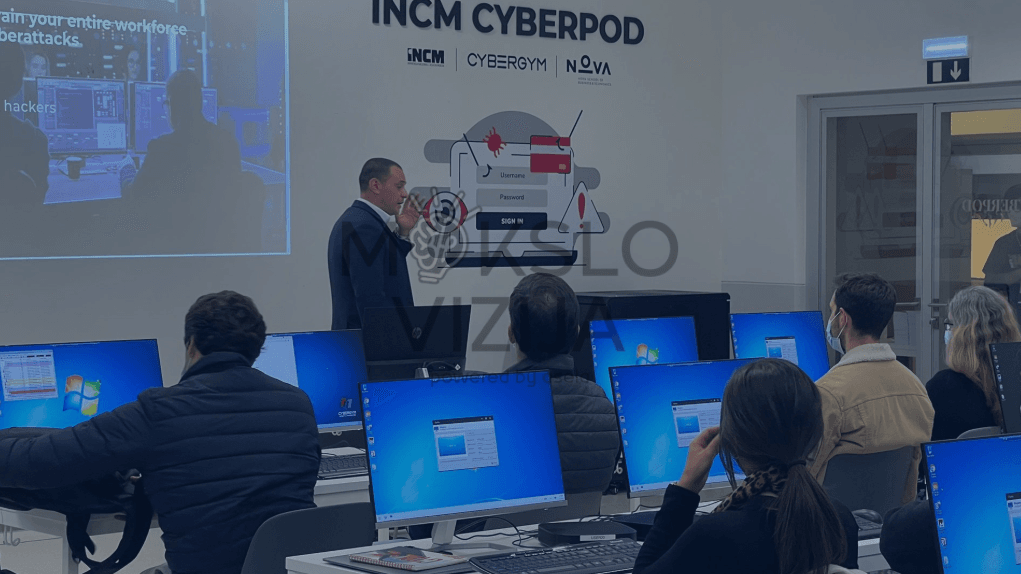 Instruktorius veda kibernetinio saugumo mokymus auditorijoje, kur dalyviai dirba su kompiuterinėmis sistemomis.