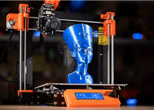 3D spausdintuvas spausdina mėlyną detalų modelį ant spausdinimo platformos, matomas ekstruderis ir valdymo ekranas.