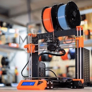 FDM 3D spausdintuvas su filamento ritėmis, pastatytas dirbtuvėse ant stalo, matomas spausdinimo mazgas.