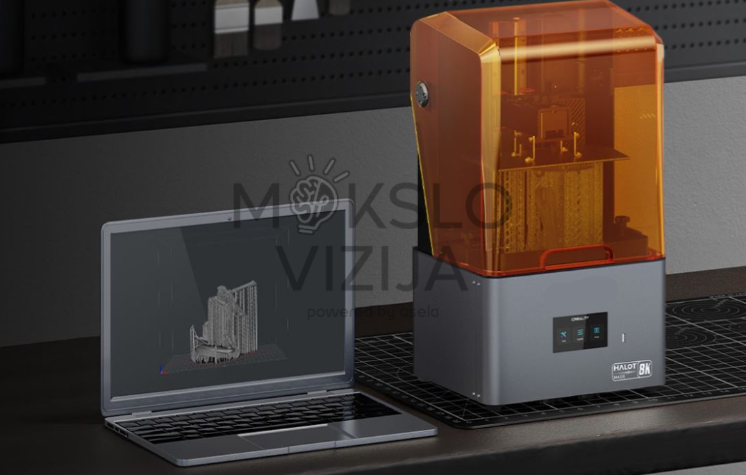 Creality HALOT-MAGE 8K dervos 3D spausdintuvas su oranžiniu dangčiu pastatytas ant stalo šalia nešiojamo kompiuterio, kurio ekrane matomas 3D modelio paruošimas.
