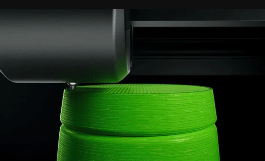 FDM 3D spausdinimo galvutė spausdinanti didelį žalią cilindrinį objektą, demonstruojanti tolygų sluoksnių klojimą ir paviršiaus kokybę.