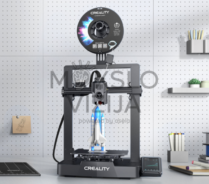 FDM 3D spausdintuvas ant stalo, viršuje filamento ritė, viduje spausdinamas raketos formos modelis, šalia valdymo ekranas.