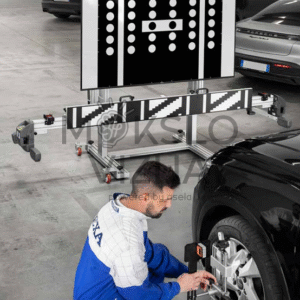 ADAS kalibravimo stendas su dideliu juodai baltu taikiniu automobilių servise, technikas reguliuoja automobilio jutiklius priekinėje dalyje.