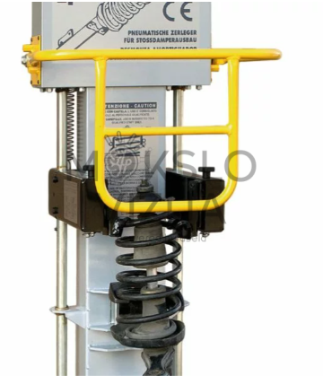 Spyruoklių suspaudimo preso mechanizmas su pritvirtintu amortizatoriumi ir spyruokle, apsaugotas metaliniu saugos rėmu.