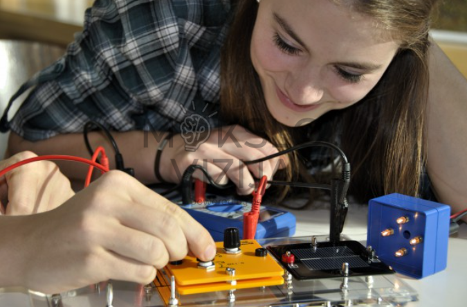 Mokinė matuoja įtampą saulės elemento eksperimente naudodama multimetrą ir jungiamuosius laidus laboratorinėje aplinkoje.