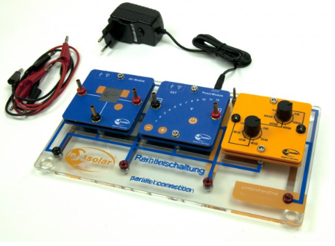 Surinkta saulės energijos bandymų schema ant skaidrios plokštės su prijungtais moduliais, maitinimo šaltiniu ir matavimo laidais.