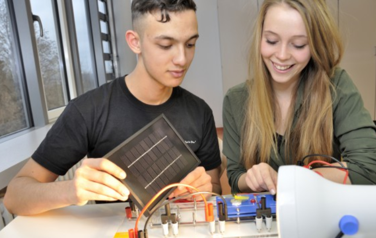 Du studentai atlieka saulės energijos eksperimentą su fotovoltiniu moduliu ir mokomąja sistema.