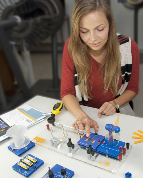 Studentė atlieka vėjo energijos eksperimentą su mokomąja turbina, moduliniais komponentais ir vėjo greičio matuokliu.