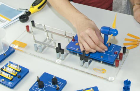 Vėjo turbinos mokomoji platforma su mėlynais moduliais, rotoriaus mentėmis ir matavimo įranga laboratoriniams eksperimentams.