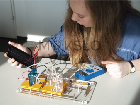 Studentė atlieka fotovoltinį eksperimentą su saulės moduliu, laboratorine baze ir skaitmeniniu matavimo prietaisu.