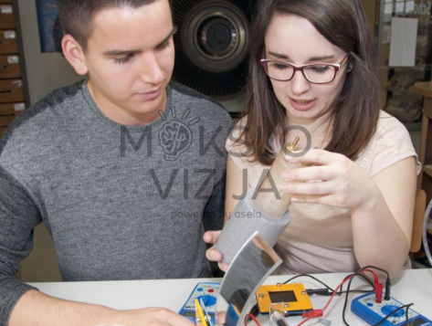 Du studentai atlieka saulės šiluminės energijos eksperimentą su kolektoriumi ir matavimo įranga laboratorijoje.