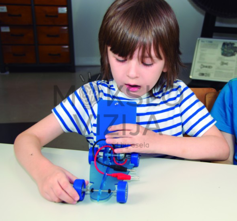 Vaikas atlieka saulės energijos eksperimentą su mini automobiliu ir mokomuoju saulės moduliu.