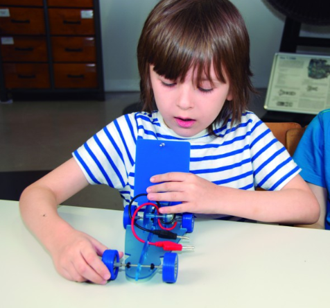 Vaikas atlieka saulės energijos eksperimentą su mini automobiliu ir mokomuoju saulės moduliu.