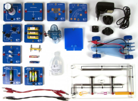 Elektromobilumo mokymo rinkinys su baterijų moduliais, kuro elemento įranga, mini automobiliu ir jungimo plokšte ant balto fono.
