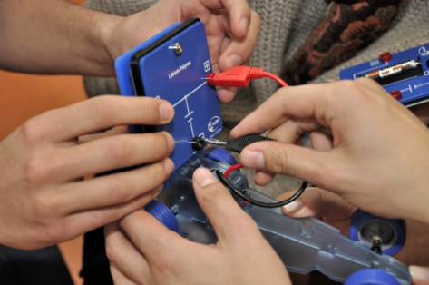 Rankos jungia energijos kaupimo modulį prie elektromobilumo automobilio modelio naudojant raudoną ir juodą laidus.