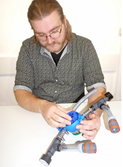 Vyras atlieka hidroenergijos eksperimentą su vandens turbinos sistema ir prijungtomis žarnomis.