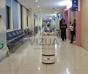 Autonominis pristatymo robotas Speedybot važiuoja ligoninės koridoriumi tarp laukiamojo zonos kėdžių.