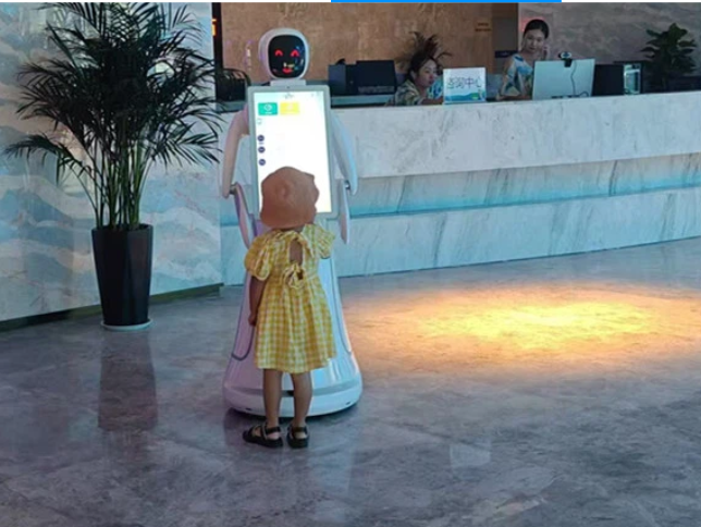 Autonominis klientų aptarnavimo robotas su liečiamu ekranu registratūros erdvėje, skirtas informacijos pateikimui ir bendravimui su lankytojais.