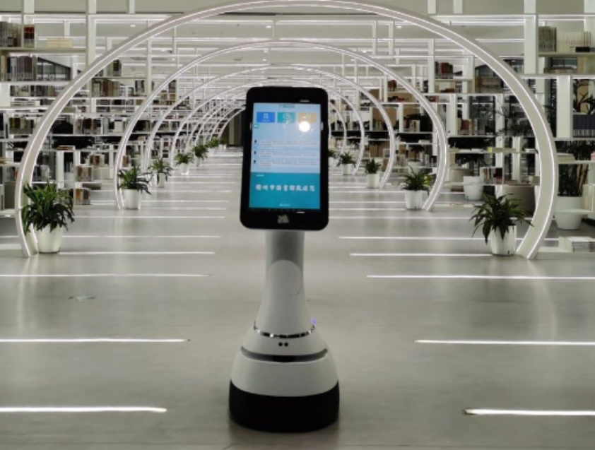 Mobilus dirbtinio intelekto serviso robotas su ekranu modernioje bibliotekoje, skirtas navigacijai ir informacijos pateikimui.