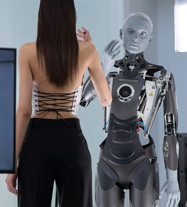 Humanoidinis robotas bendrauja su žmogumi demonstracinėje aplinkoje, rodydamas realistišką veido mimiką ir kūno judesius.