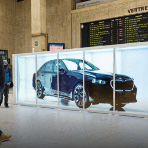Viešoje erdvėje pastatyta didelė holografinė vitrina, kurioje rodomas prabangaus automobilio vaizdas, o aplink vaikšto žmonės.