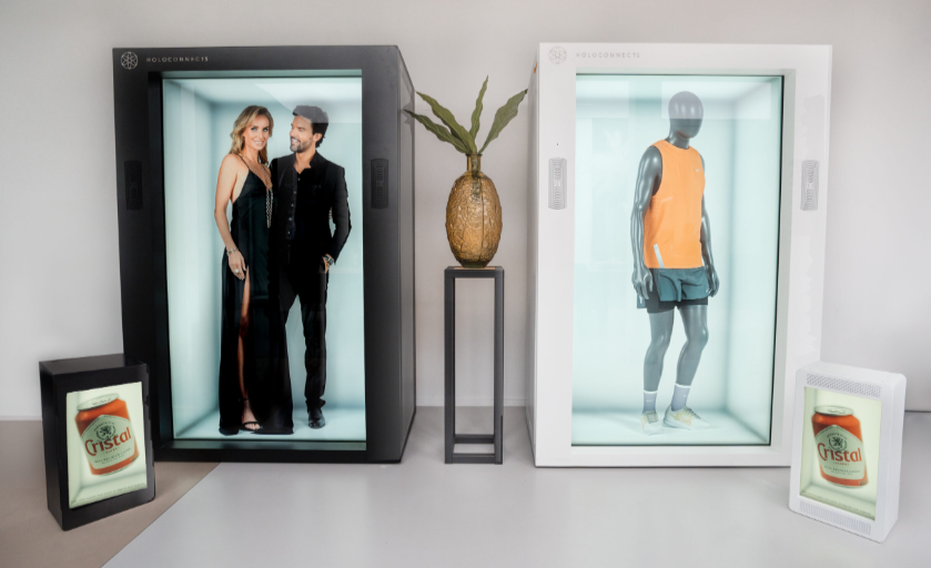 Dvi kompaktiškos holografinės vitrinos – juoda ir balta – rodo 3D žmogaus modelius bei produktų vizualizacijas modernioje interjero aplinkoje.