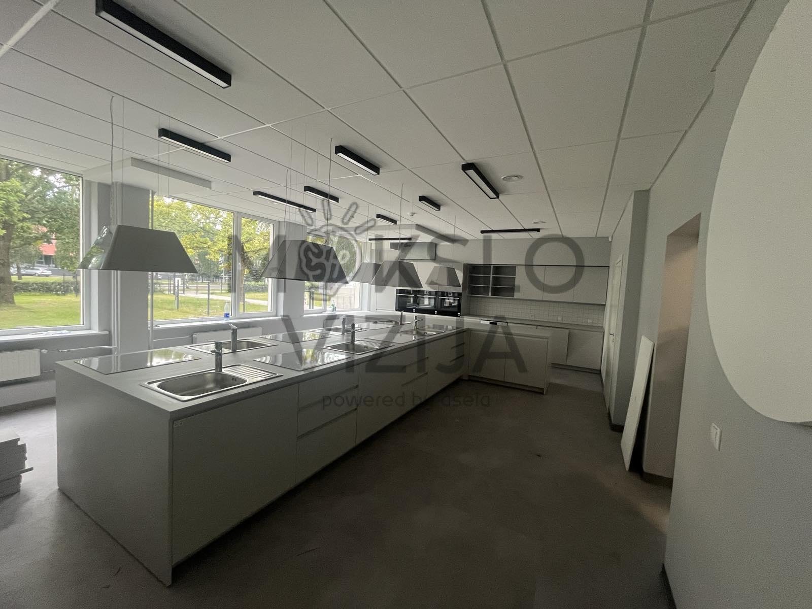 Technologijų klasė su virtuvės darbo salomis, kriauklėmis ir pakabinamomis garų ištraukimo gaubtais.