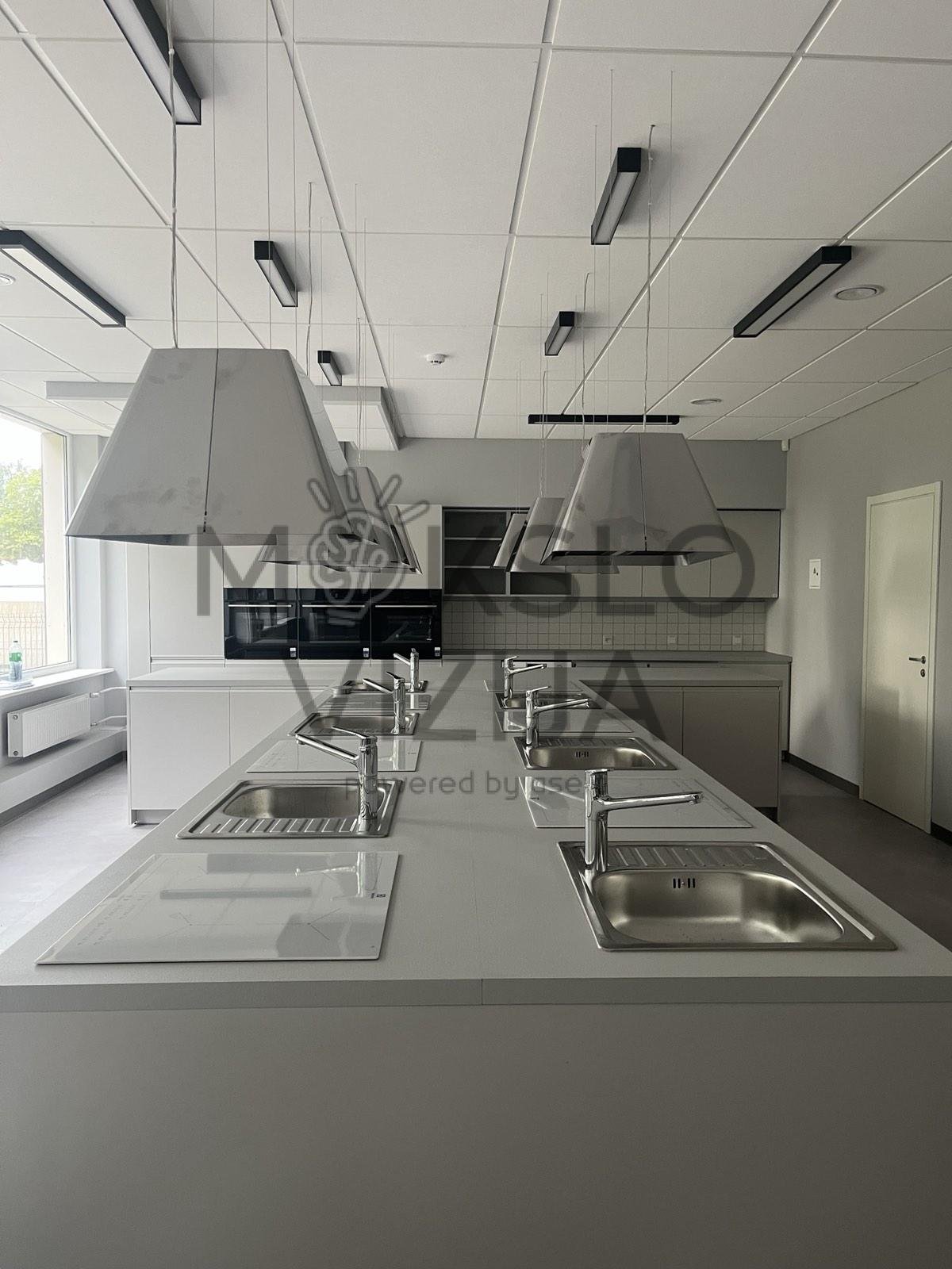 Technologijų klasė su virtuvės darbo salomis, kriauklėmis ir pakabinamomis garų ištraukimo sistemomis.