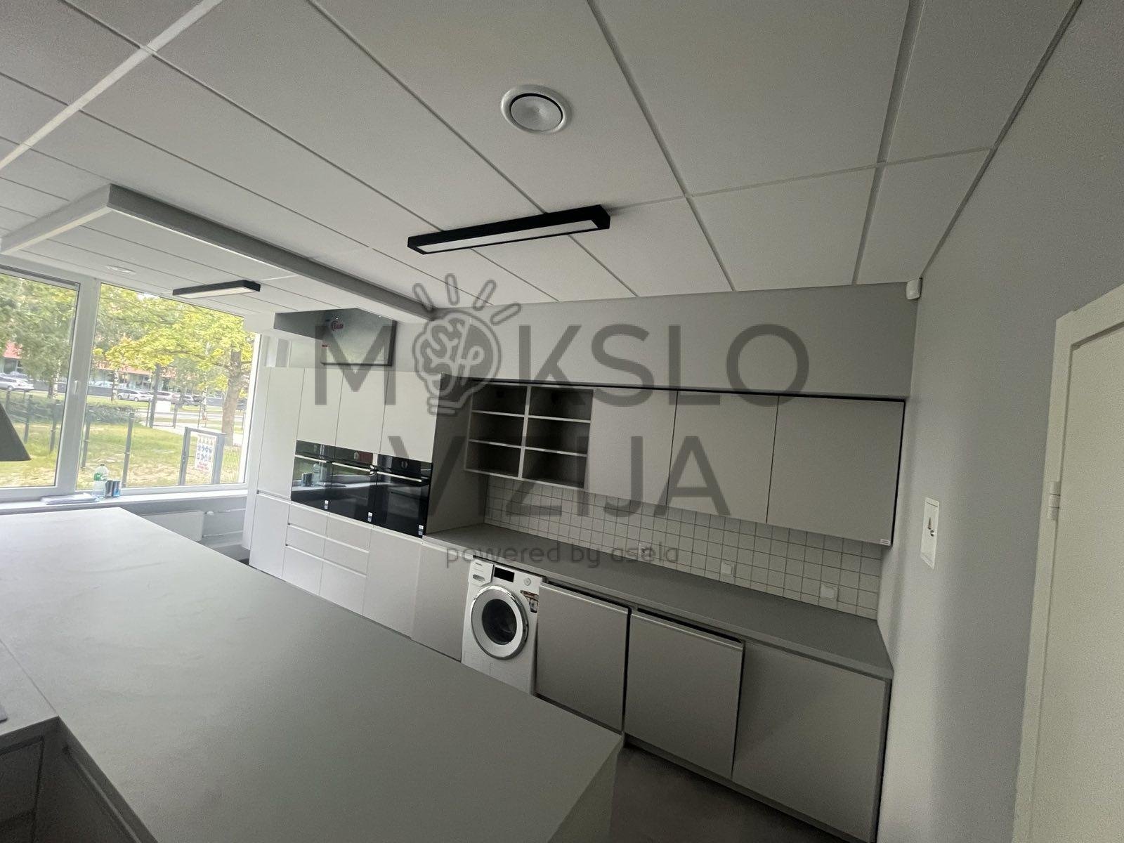 Moderni technologijų klasės virtuvės zona su spintelėmis, buitine technika ir darbo stalviršiu.