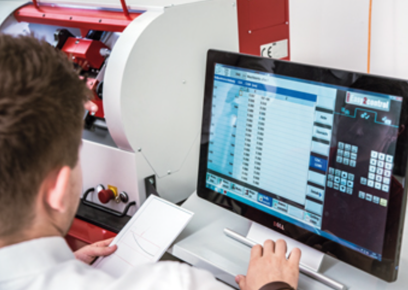 CNC tekinimo centro operatorius dirbantis su CNC valdymo sistema ir programavimo programine įranga prie kompiuterio.