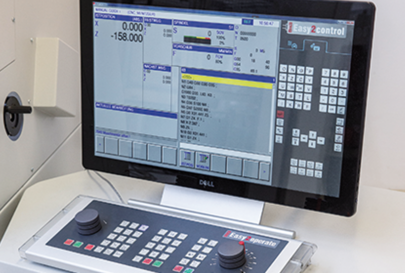 CNC staklių valdymo monitorius ir operatoriaus valdymo pultas su programavimo klaviatūra ir valdymo rankenėlėmis.