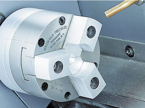 Trijų žnyplių metalo ruošinio griebtuvas CNC staklėse, skirtas tiksliai fiksuoti detales apdirbimo metu.