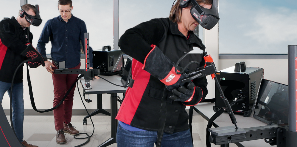 Studentai praktikuoja suvirinimą naudojant virtualios realybės suvirinimo simuliatorių mokymo laboratorijoje.