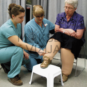 Kineziterapijos specialistės apžiūri vyresnės moters koją klinikinėje aplinkoje, vertindamos judėjimą ir galimą skausmą