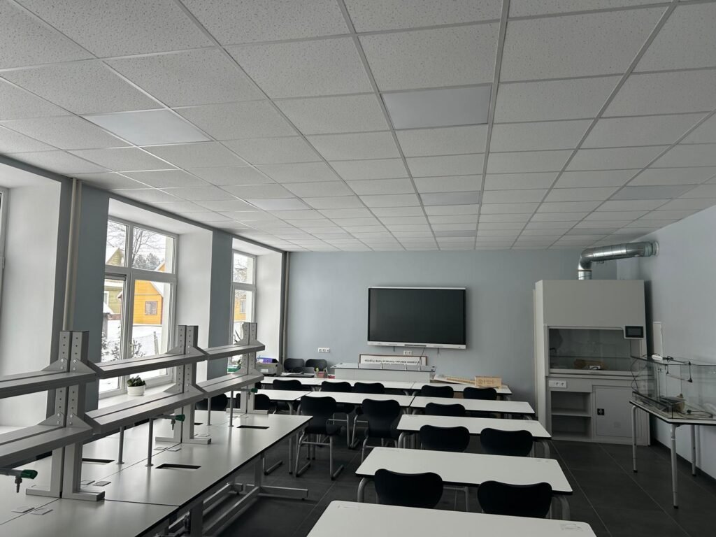 Moderni fizikos laboratorija su demonstraciniu stalu, traukos spinta ir mokinių darbo vietomis.