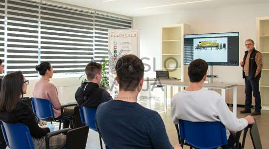 studentai klasėje stebi dėstytojo pristatymą prie ekrano su technologijų demonstracija